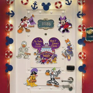 May include: A white door decorated with Disney cruise-themed magnets featuring Mickey, Minnie, Donald, Daisy, Goofy, and Pluto in Halloween costumes. A large central Mickey-shaped magnet displays the text The Smith Family 2026 Our 1st Disney Cruise.