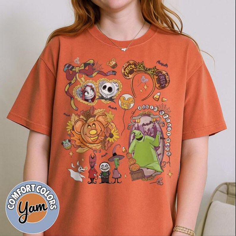Pode incluir: Uma t-shirt de manga curta em laranja queimado com uma impress&atilde;o gr&aacute;fica de personagens de O Estranho Mundo de Jack, incluindo Jack Skellington, Sally e Oogie Boogie, juntamente com &iacute;cones sazonais como ab&oacute;boras, morcegos e orelhas de rato.