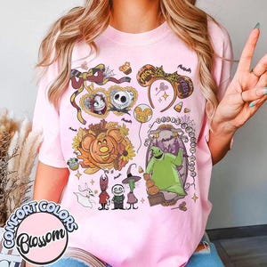Pode incluir: Uma t-shirt rosa claro com uma estampa gr&aacute;fica de personagens e &iacute;cones de O Estranho Mundo de Jack. O design inclui Jack Skellington, Sally, Oogie Boogie, Zero e v&aacute;rios elementos sazonais como ab&oacute;boras e orelhas de rato.