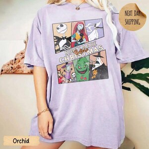 May include: A light purple short-sleeve t-shirt featuring a graphic print of characters from The Nightmare Before Christmas. The design includes panels of Jack Skellington, Sally, Zero, and Oogie Boogie with the text Nightmare Before Christmas.