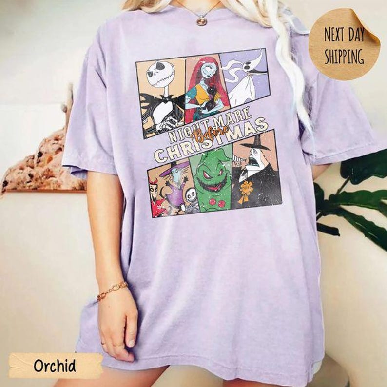 May include: A light purple short-sleeve t-shirt featuring a graphic print of characters from The Nightmare Before Christmas. The design includes panels of Jack Skellington, Sally, Zero, and Oogie Boogie with the text Nightmare Before Christmas.