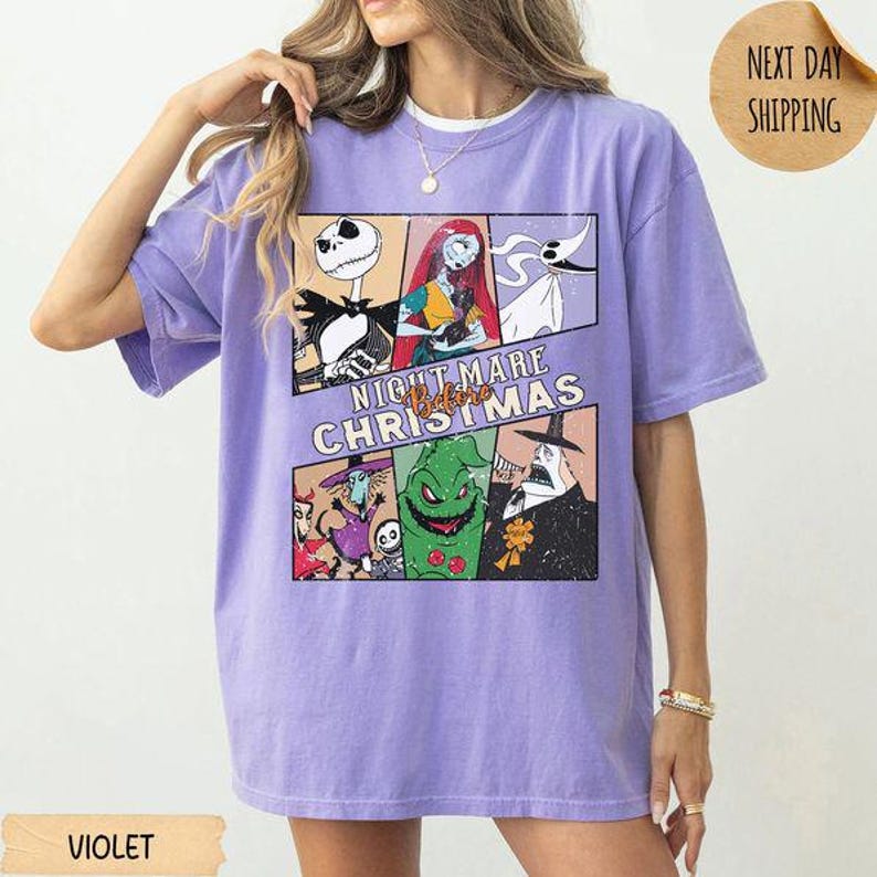 May include: A violet short-sleeve t-shirt featuring a graphic print of characters from The Nightmare Before Christmas. The design includes Jack Skellington, Sally, Zero, Oogie Boogie, and the Mayor, with the text "NIGHTMARE BEFORE CHRISTMAS".