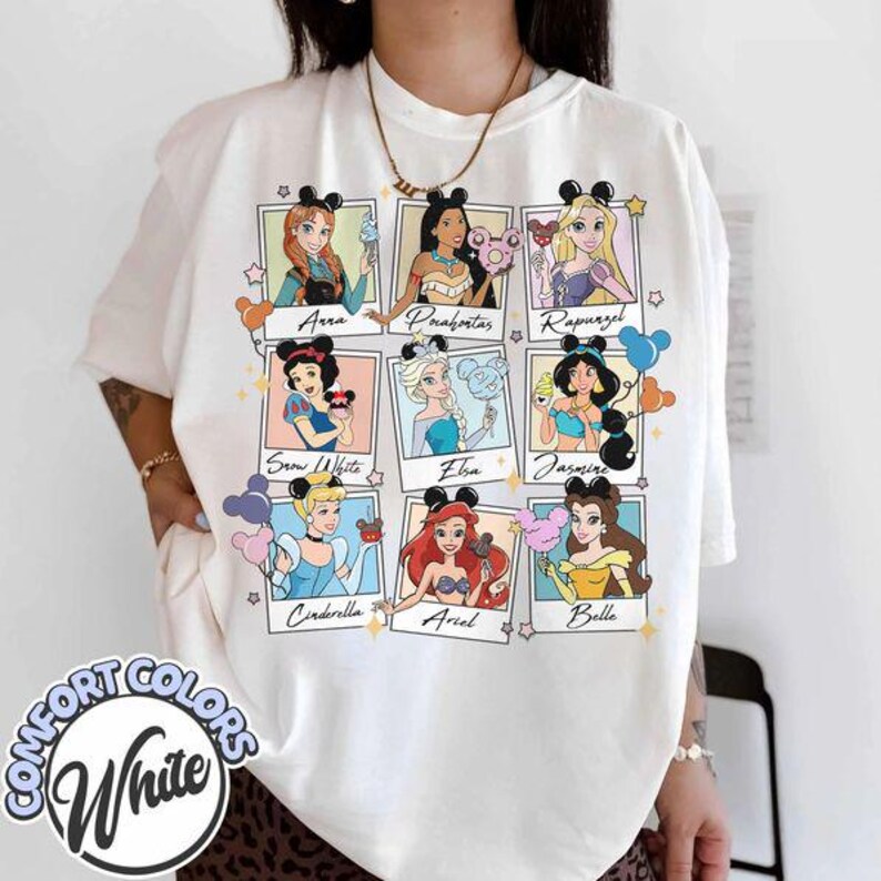 May include: White Comfort Colors t-shirt featuring nine Disney princesses in framed portraits. Each princess is depicted with a cotton candy treat and wearing mouse ears. The princesses include Anna, Pocahontas, Rapunzel, Snow White, Elsa, Jasmine, Cinderella, Ariel, and Belle.