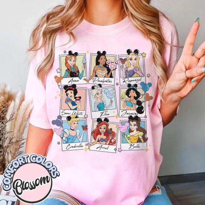 May include: Pink Comfort Colors t-shirt featuring a collage of Disney princesses in polaroid-style frames. Each princess is depicted with a unique accessory. The shirt includes the text "Comfort Colors Blossom" in a circular design.