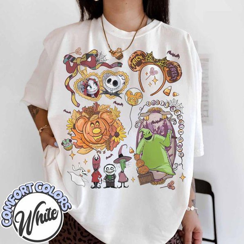 Pode incluir: Uma t-shirt branca com uma impress&atilde;o gr&aacute;fica colorida de personagens e &iacute;cones de O Estranho Mundo de Jack, incluindo Jack Skellington, Sally, Oogie Boogie, Zero e v&aacute;rios motivos sazonais como ab&oacute;boras e teias de aranha.