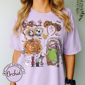 Pode incluir: Uma t-shirt roxo-claro com uma estampa gr&aacute;fica de personagens e &iacute;cones de O Estranho Mundo de Jack, incluindo Jack Skellington, Sally, Oogie Boogie e Zero, rodeados por folhas de outono, doces de milho e tiaras de orelhas de rato.
