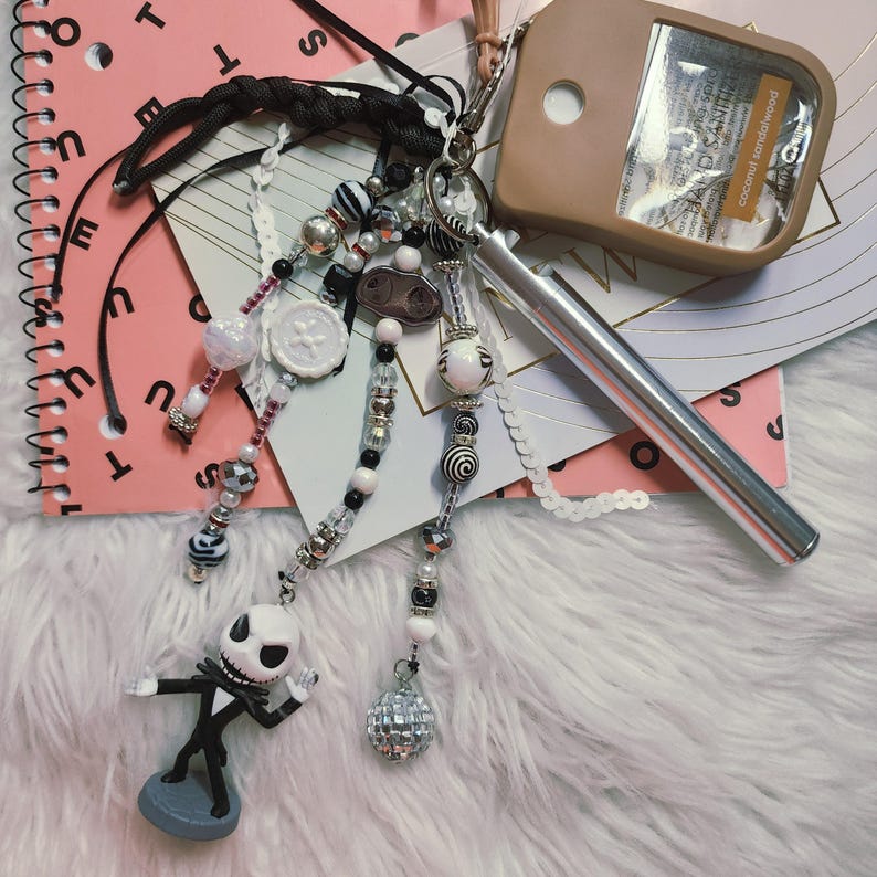 Puede incluir: Un accesorio de llavero que presenta una figura del personaje Jack Skellington, un bol&iacute;grafo de metal plateado y un soporte para desinfectante de manos color canela etiquetado como coconut sandalwood. Incluye varias hileras de cuentas con patrones.