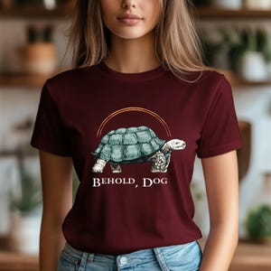 May include: A maroon t-shirt with a graphic of a turtle walking with the text "Behold, Dog" printed on the front.