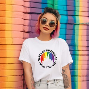 May include: White t-shirt with a rainbow graphic of a castle and the text "MAKES NO DIFFERENCE WHO YOU ARE" in a circular design. The shirt is worn by a person with pink hair and sunglasses, standing in front of a colorful wall.