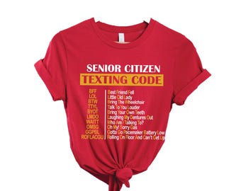 May include: Red t-shirt with the text "SENIOR CITIZEN TEXTING CODE" in white and yellow. The shirt features a list of texting acronyms and their meanings, such as "BFF" for "Best Friend Fell".