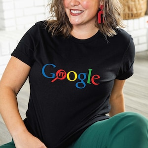 May include: Black t-shirt with the word "Google" in the Google logo colors: blue, red, yellow, and green. The word "IT" is in red, replacing the "o" in Google. The shirt is worn with green pants.