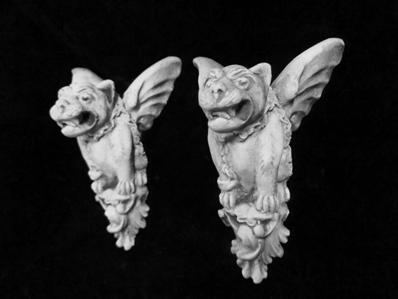 May include: Two white stone gargoyle sculptures with wings, each with a snarling expression and detailed carvings.