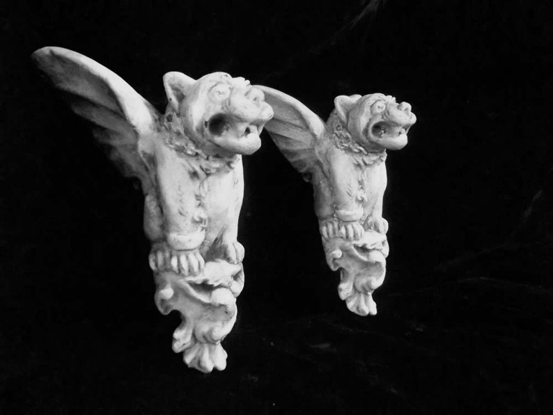 May include: Two white gargoyle sculptures with wings, each with a detailed face and a textured base.