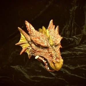 May include: A red and gold dragon head sculpture with a textured surface and open mouth. The sculpture is made of ceramic and has a realistic appearance.
