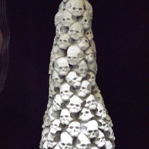May include: A white sculpture of a tall, conical stack of human skulls.