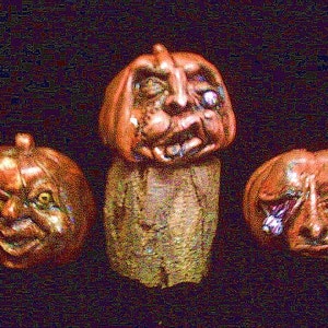 May include: Three ceramic pumpkins with grotesque faces. The pumpkins are painted in shades of orange and brown.
