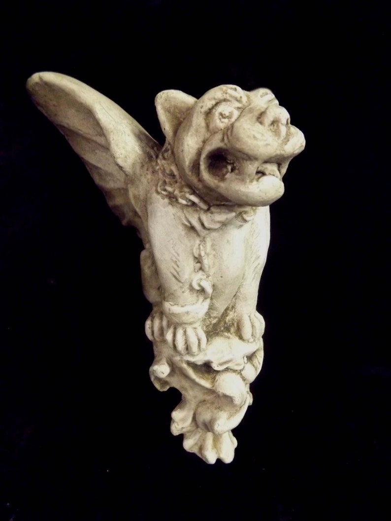 May include: A white stone gargoyle sculpture with wings, a snarling face, and a detailed design. The gargoyle is perched on a stone base.