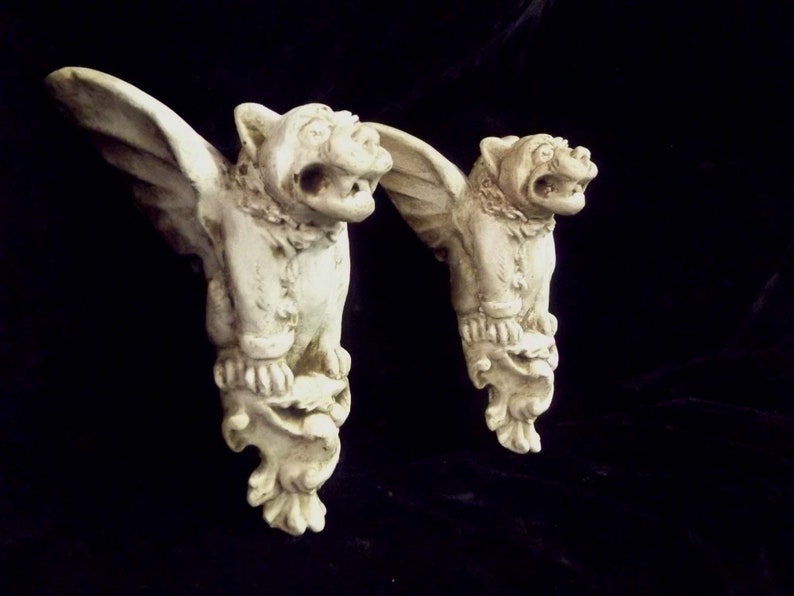 May include: Two white gargoyle wall sculptures with wings, each with a detailed face and a textured base.