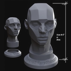 May include: A grey, geometric sculpture of a human head, approximately 15cm tall, with a base that reads "Engraved Personalisation." A smaller head and a ring-shaped base are also present. The sculpture has a modern, angular design.