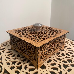 May include: A wooden box with intricate cutouts and a silver knob on the top. The box is sitting on a wooden surface with a similar design.