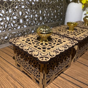 Puede incluir: Dos cajas de madera tallada intrincadamente con manijas de metal dorado ornamentadas. Las cajas tienen un patrón geométrico y están hechas de madera marrón claro.