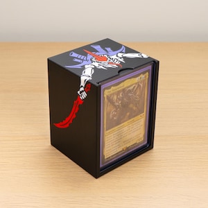 May include: A black rectangular trading card deck box featuring a graphic of a white, purple, and red creature holding a curved red blade. The front of the box has a clear window displaying a gold-bordered trading card titled The Swarmlord.