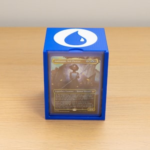 Könnte beinhalten: Eine blaue Sammelkarten-Deckbox aus Kunststoff mit einem weißen Wassertropfen-Symbol auf dem Deckel. Die Vorderseite der Box hat ein durchsichtiges Fenster, in dem eine Magic: The Gathering-Karte mit dem Titel Aminatou, Veil Piercer zu sehen ist.