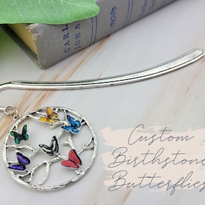 May include: Silver bookmark with a circle charm featuring a tree with six colourful butterflies. The text "Custom Birthstone Butterflies" is written below the charm.