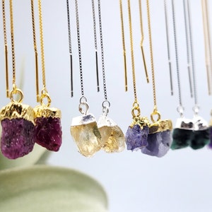 May include: A set of 10 pairs of gold and silver dangle earrings with different colored crystal stones. The stones are raw and have a natural, rough texture. The earrings are delicate and feminine.