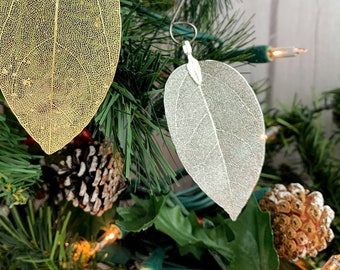 May include: Two delicate leaf ornaments, one gold and one silver, hanging on a Christmas tree. The leaves are translucent and have a delicate vein pattern.