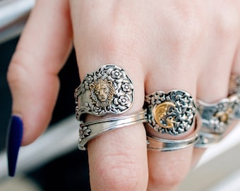 May include: A hand wearing several silver rings with ornate designs. The rings feature a lion, a crescent moon, and other decorative elements.