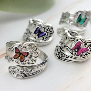 May include: Five silver rings with butterfly designs. Each ring features a different colored butterfly with intricate details. The rings are made from vintage silverware.