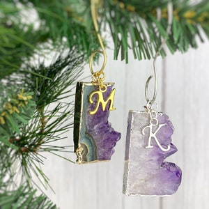 May include: Two amethyst crystal ornaments with gold and silver trim. The ornaments are shaped like a rectangle and a freeform shape. The ornaments have a gold letter "M" and a silver letter "K" attached to them.