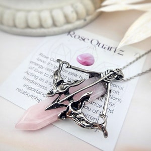 May include: A silver pendant necklace with a rose quartz crystal in a decorative cage design. The pendant is on a white card with the text "Rose Quartz 7".