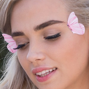 May include: A woman with long blonde hair wearing a white lace off-the-shoulder top. She has pink butterfly hair clips on each side of her head.