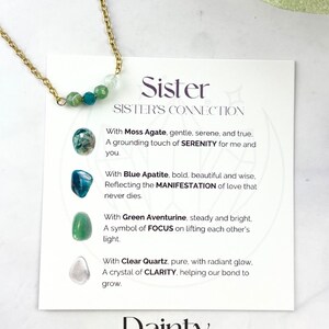 Może przedstawiać: Złoty naszyjnik z kartą, na kt&oacute;rej napisano "Siostra, Połączenie si&oacute;str". Karta opisuje znaczenie każdego kamienia szlachetnego: agatu mchowego, apatytu niebieskiego, awenturynu zielonego i czystego kwarcu. Naszyjnik ma długość 35,5 cm z przedłużką 5 cm i zawiera kamienie szlachetne o średnicy 4 mm. Na karcie widnieje r&oacute;wnież napis "Delikatny, Kamienie szlachetne 4 mm, Łańcuszek 35,5 cm + przedłużka 5 cm".