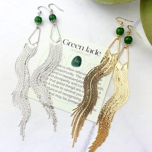 May include: A pair of long, dangling earrings with green jade stones and gold and silver chain fringe. The earrings are displayed on a card with the text "Green Jade Opportunity".
