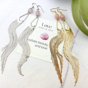May include: A pair of long, dangling earrings with rose quartz stones and a chain tassel. The earrings are available in silver and gold. The card reads "Love Rose Quartz radiate beauty and love."