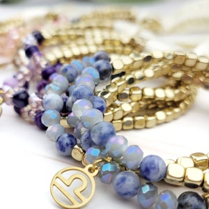May include: A set of bracelets with blue and purple beads, gold beads, and gold charms with zodiac symbols. The charms are for the signs of Pisces and Libra.
