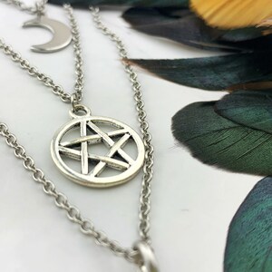 Pu&ograve; includere: Una collana argentata a strati con tre ciondoli. Lo strato superiore ha una luna crescente, quello centrale un pentagramma all'interno di un cerchio e quello inferiore un ciondolo circolare. Le catene sono delicate e i ciondoli hanno una finitura antica.