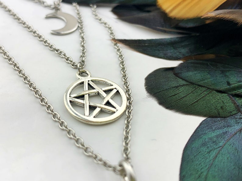 Pu&ograve; includere: Una collana argentata a strati con tre ciondoli. Lo strato superiore ha una luna crescente, quello centrale un pentagramma all'interno di un cerchio e quello inferiore un ciondolo circolare. Le catene sono delicate e i ciondoli hanno una finitura antica.