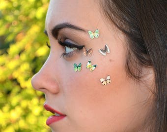 May include: A close-up of a woman's face with several small butterfly stickers applied to her cheek and forehead. The butterflies are in various colors, including green, blue, and brown.