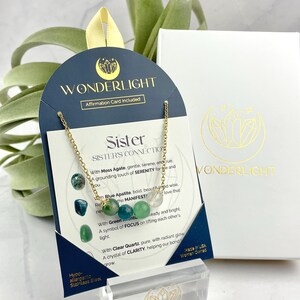 Może przedstawiać: Złoty naszyjnik z zielonymi, niebieskimi i przezroczystymi koralikami z kryształu. Naszyjnik jest prezentowany na kartce z tekstem "Sister's Connection" i opisami kamieni. Kartka jest oznaczona jako "Wonderlight".