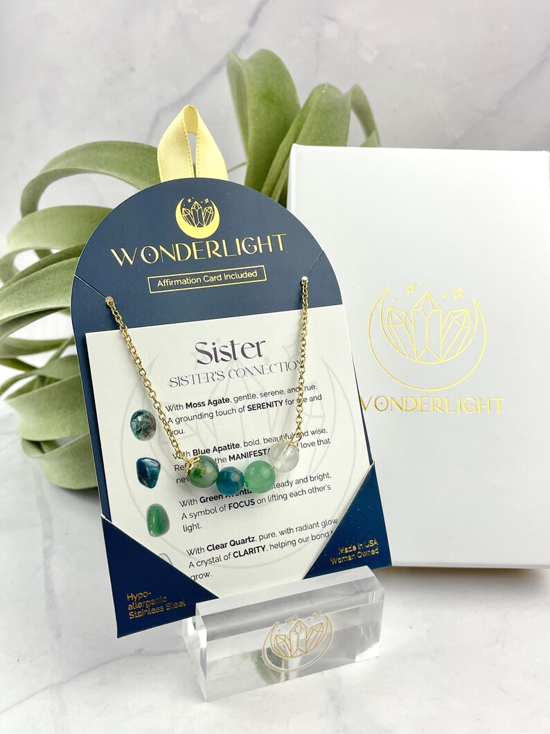 Może przedstawiać: Złoty naszyjnik z zielonymi, niebieskimi i przezroczystymi koralikami z kryształu. Naszyjnik jest prezentowany na kartce z tekstem "Sister's Connection" i opisami kamieni. Kartka jest oznaczona jako "Wonderlight".