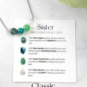 Może przedstawiać: Srebrny naszyjnik z czterema kamieniami szlachetnymi: agatem mchowym, apatytem niebieskim, aventurynem zielonym i czystym kwarcem. Naszyjnik jest prezentowany na białej kartce z tekstem "Sister Sister's Connection" i opisami każdego kamienia szlachetnego. Na kartce widnieje r&oacute;wnież napis "Classic 8mm Gemstones 18in Chain + 2in Extender".