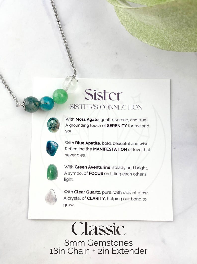 Może przedstawiać: Srebrny naszyjnik z czterema kamieniami szlachetnymi: agatem mchowym, apatytem niebieskim, aventurynem zielonym i czystym kwarcem. Naszyjnik jest prezentowany na białej kartce z tekstem "Sister Sister's Connection" i opisami każdego kamienia szlachetnego. Na kartce widnieje r&oacute;wnież napis "Classic 8mm Gemstones 18in Chain + 2in Extender".