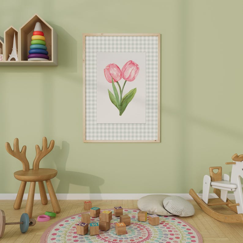 May include: Watercolor painting of two pink tulips with green leaves in a wooden frame. The artwork is set against a gray and white checkered background. The frame is hanging on a light green wall in a child's room.