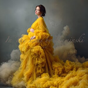 Puede incluir: Una mujer con un vestido de maternidad amarillo fluido con una falda y mangas con volantes en capas. El vestido tiene una larga cola y está sobre un fondo gris ahumado. El texto "In the Lens by Kaminski" es visible.