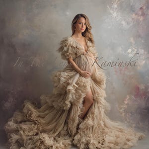 Puede incluir: Un vestido de maternidad beige con escote pronunciado y detalles de volantes. El vestido presenta una abertura alta y una cola fluida. La imagen incluye el texto "In The Lens by Kaminski".