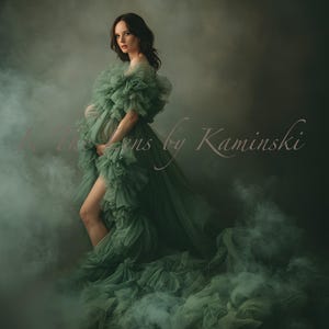 May include: A woman in a sage green maternity gown with a ruffled bodice and flowing train. The dress is made of a soft, sheer fabric. The image has a dreamy, ethereal quality, with a smoky background. Text on the image reads "In The Lens by Kaminski".